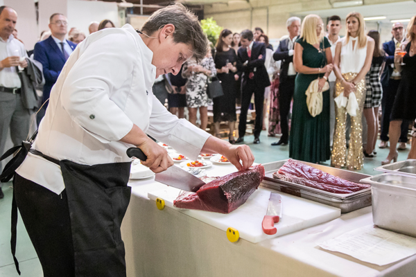 Chef taglia un grande trancio di carne rossa davanti a un gruppo di persone durante un evento