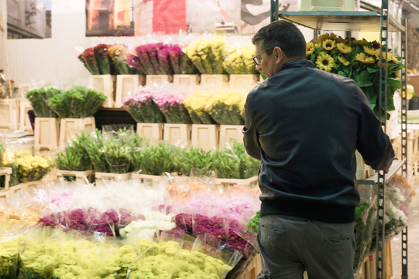 Persona che sistema mazzi di fiori colorati su uno scaffale al mercato fiori