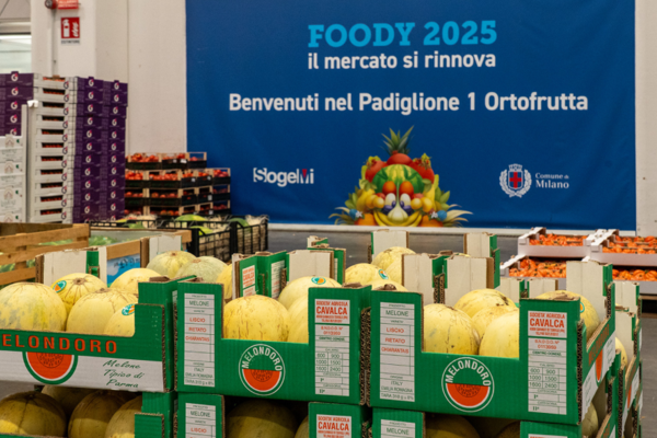 Casse di meloni nel Padiglione 1 Ortofrutta del Mercato Foody di Milano, con il banner “Foody 2025 – Il mercato si rinnova” sullo sfondo